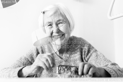 Image of Cheerful elderly 96 years old woman sitting at table at home happy with her pension savings in her wallet after paying bills. Black and white.