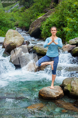 Image of Woman in yoga asana Vrikshasana tree pose at waterfall outdoors