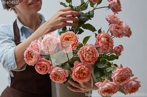 Image of Florist girl in a brown apron holding a vase with pink roses on 