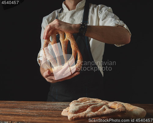 Image of on background of wooden brown table, men\'s hands hold bread fougas