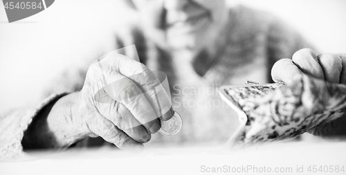 Image of Detailed closeup photo of unrecognizable elderly womans hands counting remaining coins from pension in her wallet after paying bills. Black and white image.