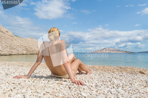 Image of Rear view of sexy young caucasian woman sunbathing topless on romote pabble beach on Pag island, Croatia, Mediterranean.