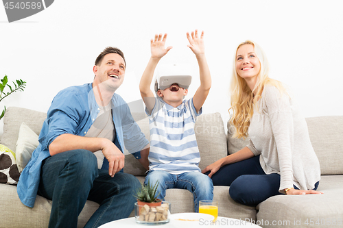 Image of Happy family at home on living room sofa having fun playing games using virtual reality headset