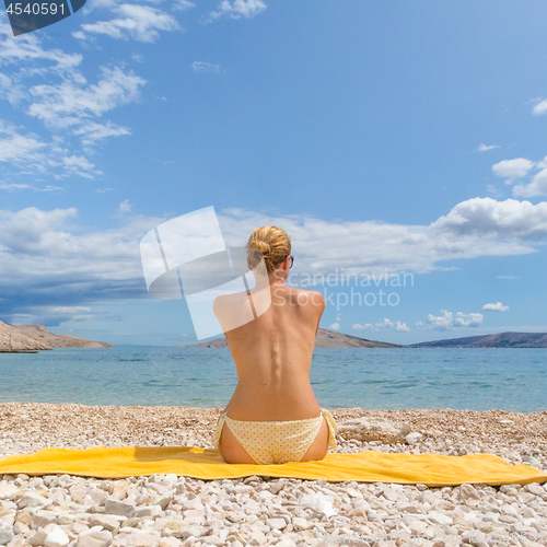 Image of Rear view of sexy young caucasian woman sunbathing topless on romote pabble beach on Pag island, Croatia, Mediterranean.