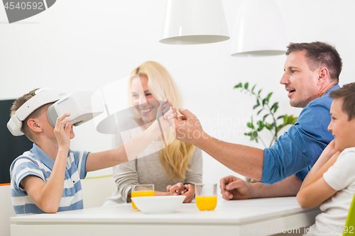 Image of Happy caucasian family at home at dinning table, having fun playing games using virtual reality headset