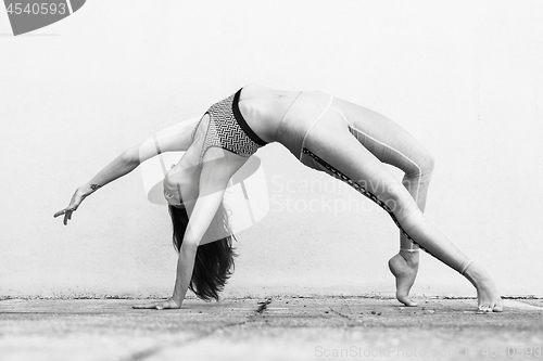 Image of Fit sporty active girl in fashion sportswear doing yoga fitness exercise in front of gray wall, outdoor sports, urban style. Black and white photo.