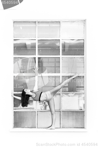 Image of Fit sporty active girl in fashion sportswear doing yoga fitness exercise in front of big industrial window frame. colorful reflections in window glass. Urban style yoga. Black and white
