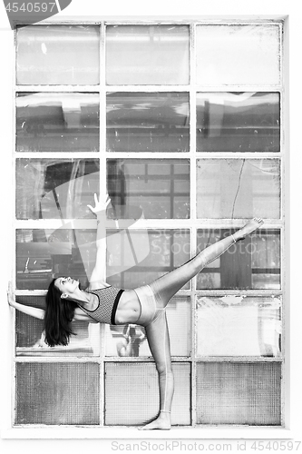Image of Fit sporty active girl in fashion sportswear doing yoga fitness exercise in front of big industrial window frame. colorful reflections in window glass. Urban style yoga. Black and white