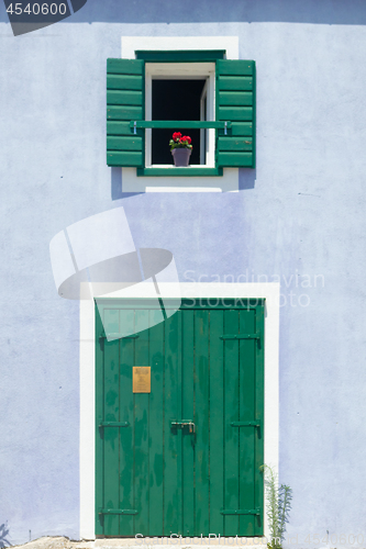 Image of Cute retro purple house with green wooden window with shutters and flowers in the pot and green door with white frame.