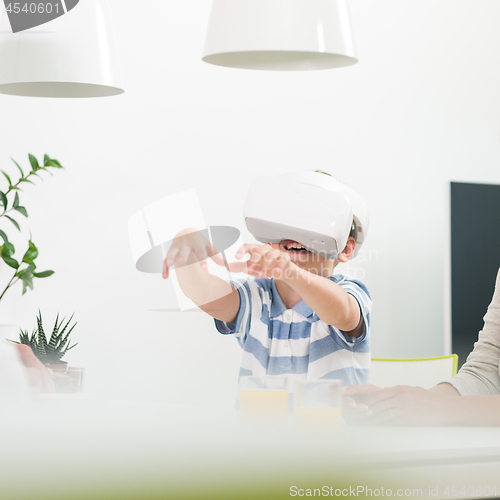 Image of Amazed child using virtual reality headsets trying to grab unexisting virtual objects while sitting at the dinner table.