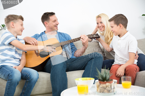 Image of Happy caucasian family smiling, playing guitar and singing songs together at cosy modern home