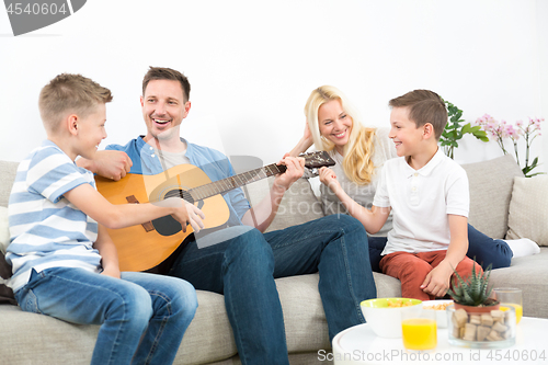 Image of Happy caucasian family smiling, playing guitar and singing songs together at cosy modern home