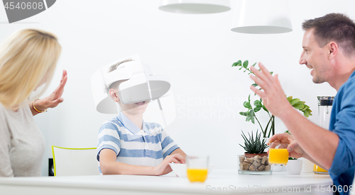 Image of Happy caucasian family at home at dinning table, having fun playing games using virtual reality headset