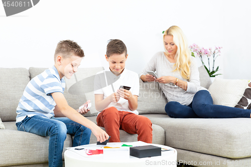 Image of Brothers playing card game on living room sofa at home supevised by their mother.