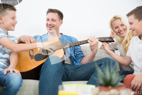 Image of Happy caucasian family smiling, playing guitar and singing songs together at cosy modern home