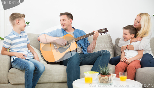 Image of Happy caucasian family smiling, playing guitar and singing songs together at cosy modern home