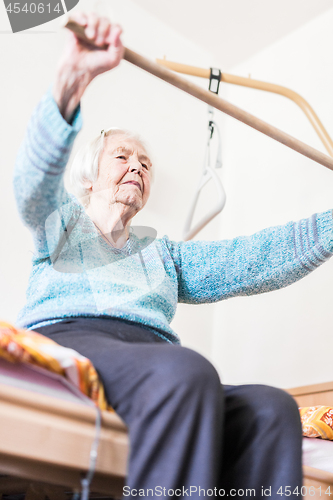 Image of Elderly 96 years old woman exercising with a stick sitting on her bad.