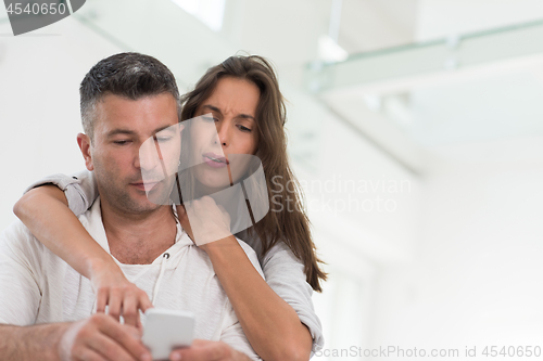 Image of happy couple using mobile phone at home