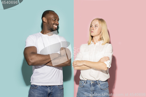 Image of Closeup portrait of young couple, man, woman. One being excited happy smiling, other serious, concerned, unhappy on pink and blue background. Emotion contrasts