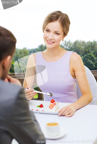 Image of woman looking at man and eating cake at restaurant