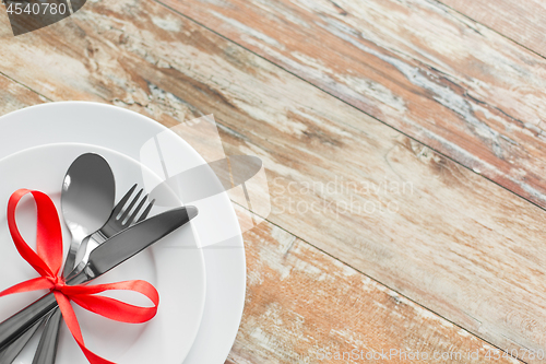 Image of cutlery tied with red ribbon on set of plates