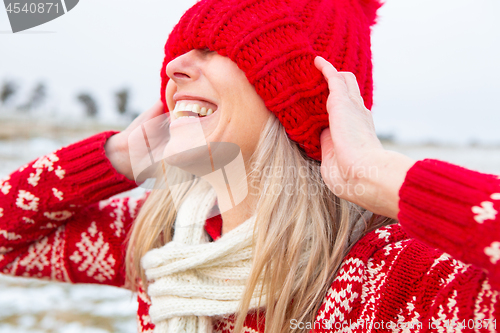 Image of Happy woman outdoors pulling beanie over eyes