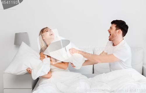 Image of happy couple having pillow fight in bed at home