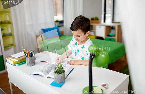 Image of student boy with book writing to notebook at home