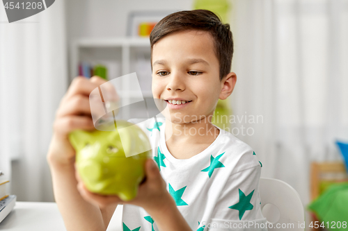 Image of little boy putting coin into piggy bank at home