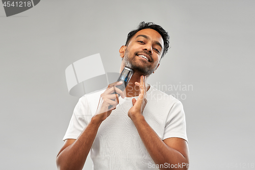 Image of smiling indian man shaving beard with trimmer