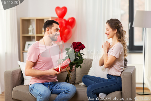Image of happy man giving woman flowers and present at home