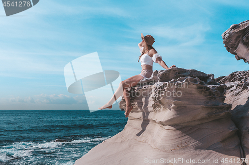 Image of Female enjoying summer sunshine, Sitting by ocean wearing sunhat