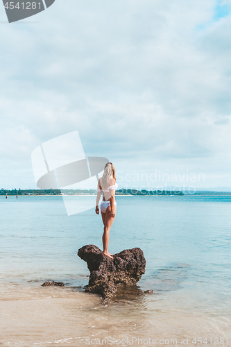 Image of Woman in bikini standing on a rock surrounded by the ocean