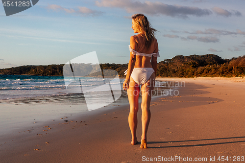 Image of Woman walking along the wet sand of the beach early morning