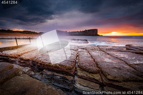 Image of Sunrise sky and waves crash onto rocky beach shore