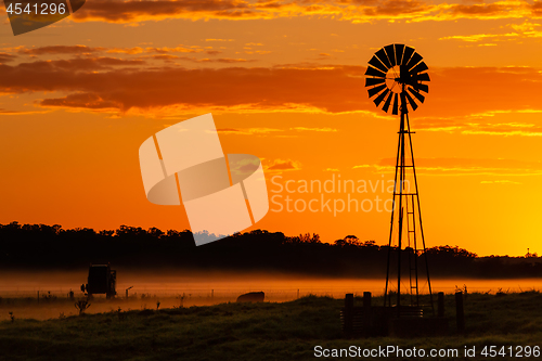 Image of Silhouette of windmill on farmland against orange yellow sky