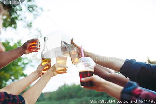 Image of Bottles of beer in people\'s hands on blue sky background