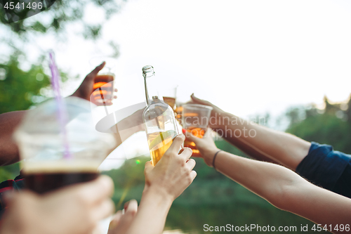 Image of Bottles of beer in people\'s hands on blue sky background