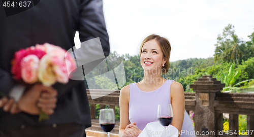 Image of woman looking at man with flowers at restaurant