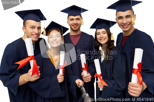 Image of happy graduates with diplomas taking selfie