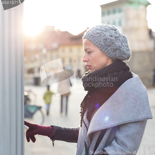Image of Casual woman buying public transport tickets on city urban vedning machine on cold winter day.
