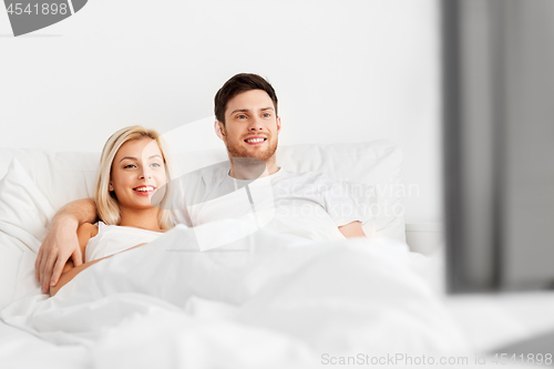 Image of happy couple lying in bed at home and watching tv