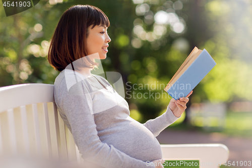 Image of happy pregnant asian woman reading book at park