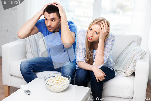 Image of upset couple with popcorn watching tv at home