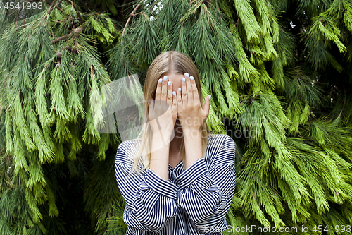 Image of Beautiful young woman hiding her face standing in the forest aga