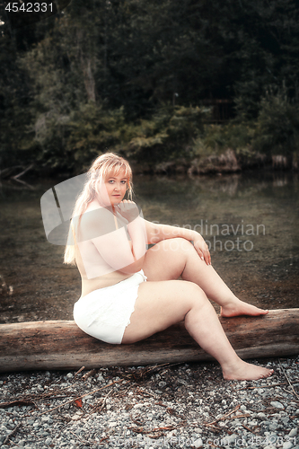 Image of Young curvy woman sits scantily clad on a lake on a tree trunk