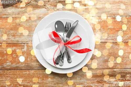 Image of cutlery tied with red ribbon on set of plates