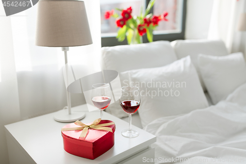 Image of gift and two glasses of wine in bedroom at home