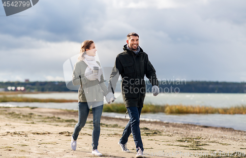 Image of couple with tumbler walking along autumn beach