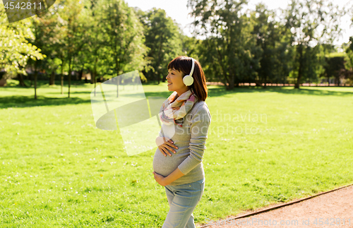 Image of happy pregnant asian woman in headphones at park